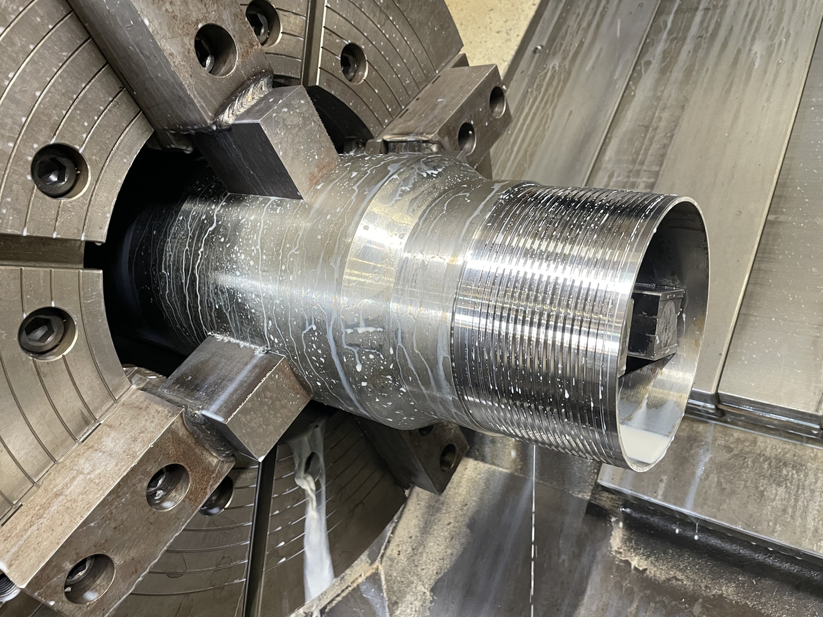 Premium OCTG connection being threaded on a CNC lathe with silver metal chips curling from the cutting edge