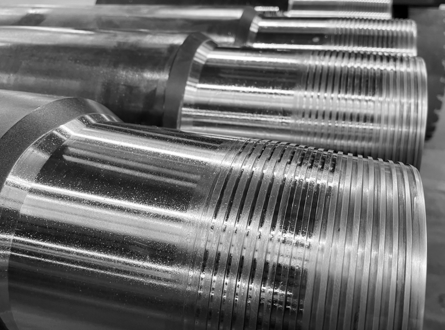 Close-up black-and-white view of premium threaded pin ends on staged casing joints