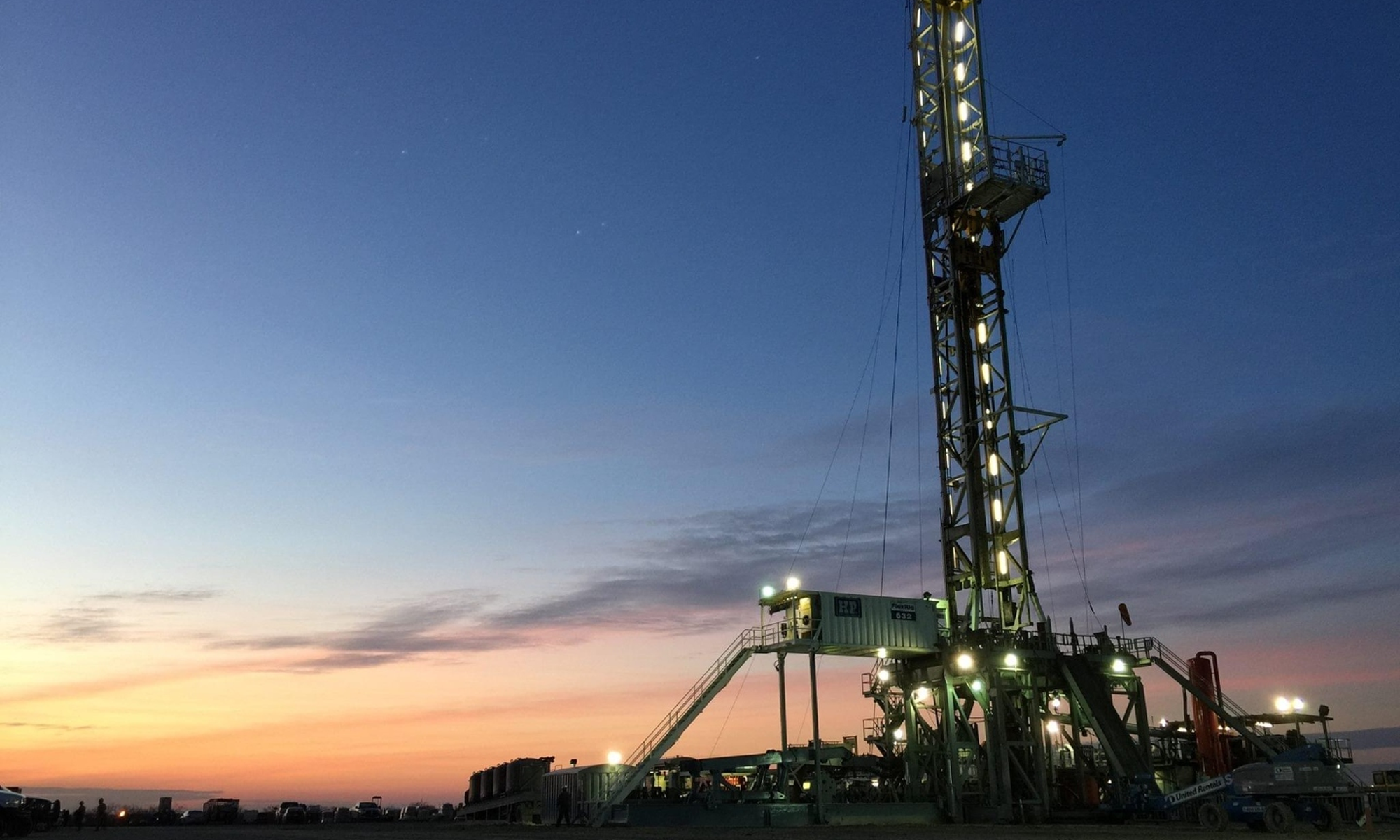 A land-based drilling rig lit up at dusk against a warm horizon — the upstream oil and gas industry Delta Solutions supplies from Magnolia, Texas