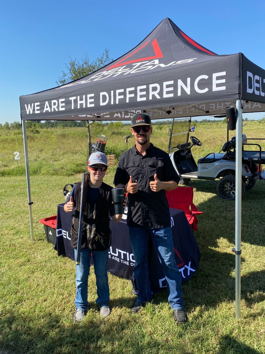 A father and son at a sporting clays event under the Delta Solutions tent