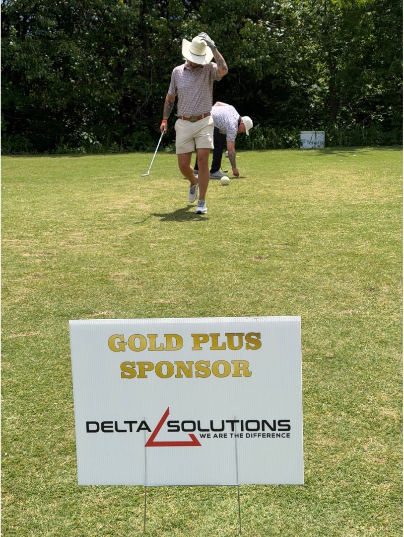 A golfer teeing off next to a Delta Solutions Gold Plus Sponsor sign