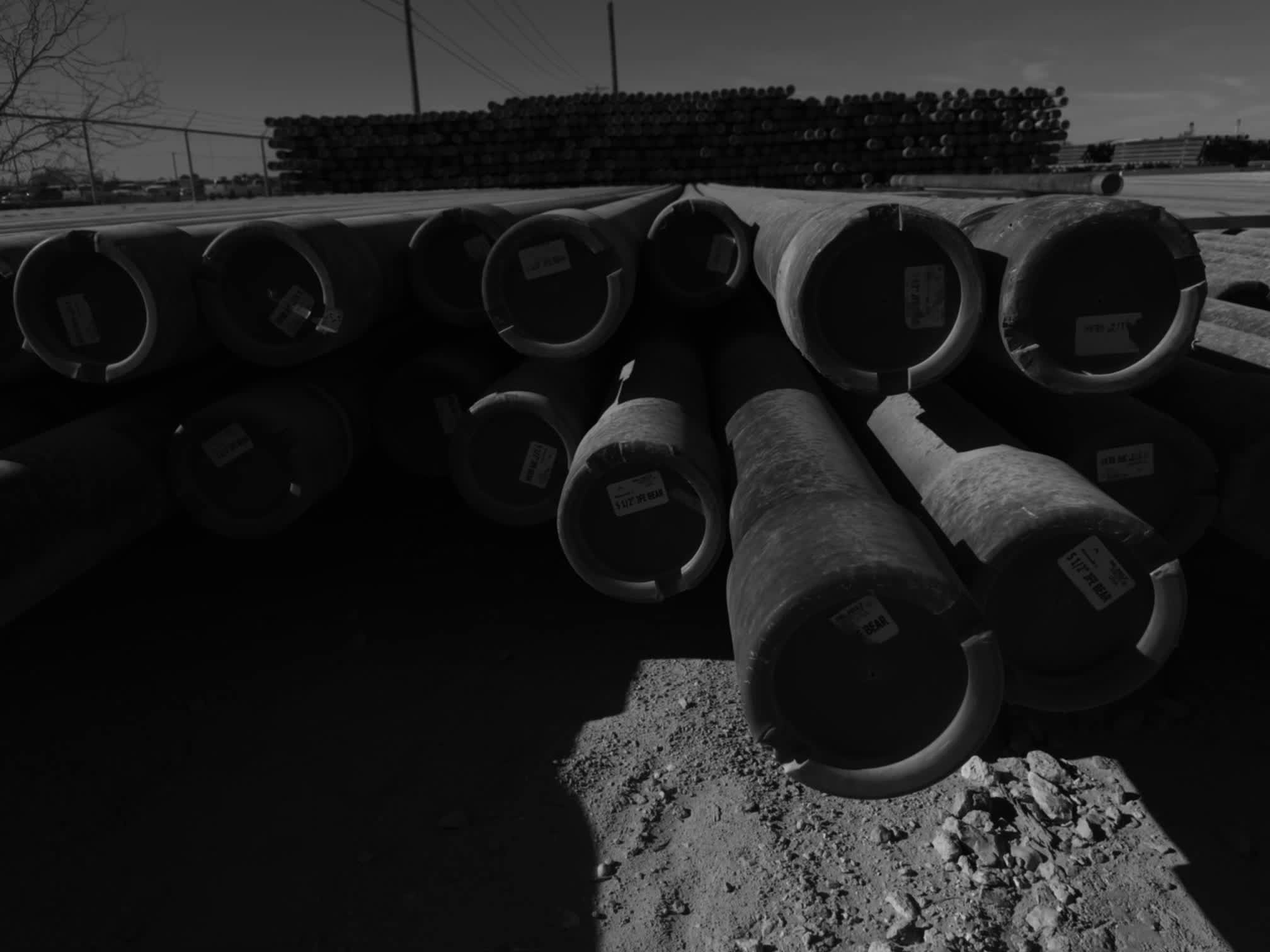 Low-angle black-and-white view of racked large-OD casing joints with tally tags in the Delta Solutions Magnolia, Texas yard