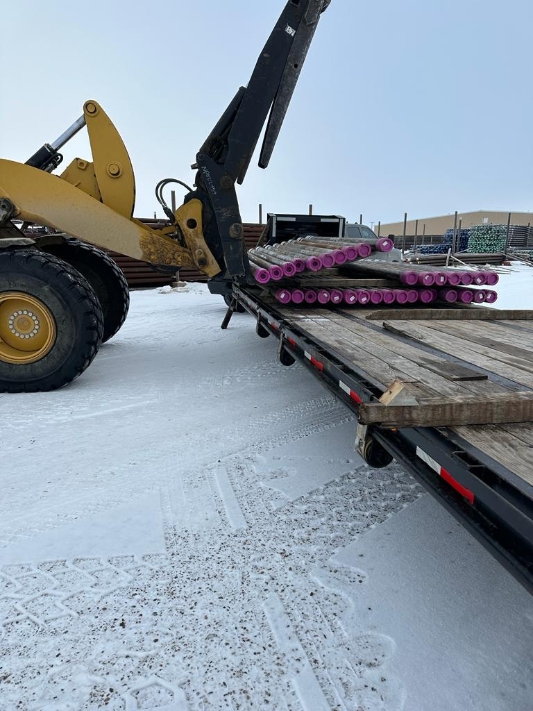 Delta Solutions loading casing with purple thread protectors onto a step-deck flatbed at a North Dakota yard